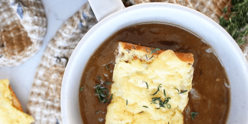 Weiße Schale mit Zwiebel-Pilzsuppe und einem Brötchen mit geschmolzenem Käse.
