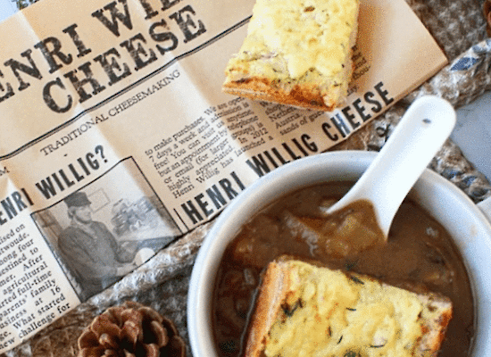 Zwiebel-Pilzsuppe serviert in einer weißen Schale mit knusprigem überbackenem Baguette und Henri Willig Bockshornkleekäse.