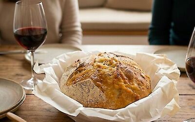 Sourdough bread in a bowl on a table with butter and glasses of wine, with two people sitting together at the table in the background