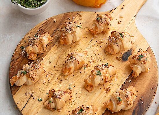 12 Mini-Croissants auf einem runden Holzbrett.