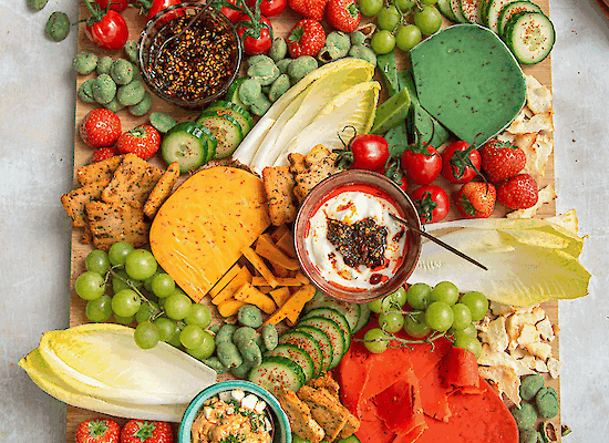 Hot & Spicy Snackplatte mit farbenfrohen Käsesorten, Trauben, Erdbeeren, Gurke, Tomaten und Dips von Henri Willig