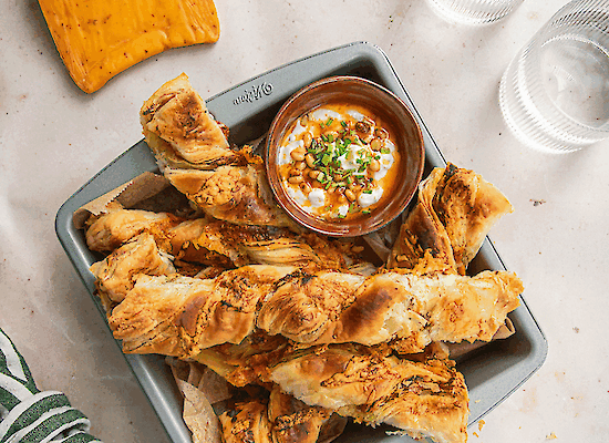 Bâtonnets de fromage au chili en pâte feuilletée avec dip au yaourt frais et beurre épicé aux pignons, dorés au four et servis en apéritif