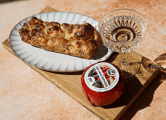 Croissant-Zupfbrot mit geschmolzenem Henri Willig Chili-Kuhkäse und Hot Honey, serviert auf einem Holzbrett mit einem Glas Wein.