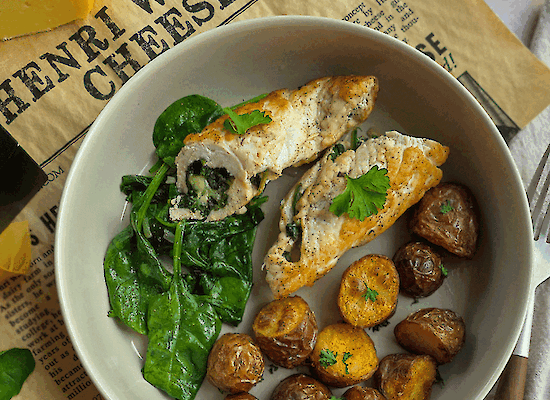 Plate with stuffed chicken rolls filled with spinach and Henri Willig Jersey cheese, served with crispy baby potatoes and fresh spinach on Henri Willig Cheese wrapping paper.