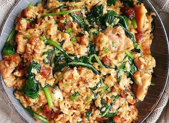 Cremiges Risotto mit Spinat, Chorizo-Stückchen und geschmolzenem Käse, serviert auf einem dunklen Teller, garniert mit frischer Petersilie.